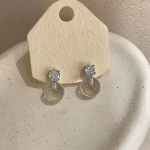 Dettaglio di eleganti orecchini a perno in argento con zirconi e sfera di vetro chiara