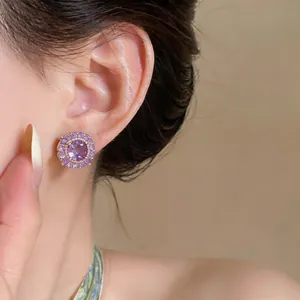 Primo piano di un orecchino a bottone tondo con zircone viola indossato all'orecchio