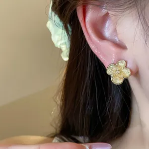 Primo piano di un elegante orecchino a fiore dorato con dettagli materici sull'orecchio
