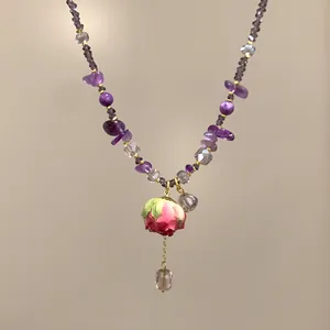 Dettaglio ravvicinato di un ciondolo rosa su una collana di perline di cristallo viola
