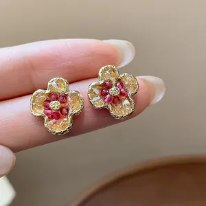 Primo piano di eleganti orecchini a lobo a fiore dorati con pietre in vetro rosso.