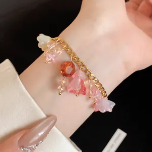 Detailopname van een armband met roze harsbloemen en gouden ketting om de pols gedragen