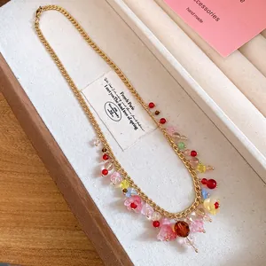 Detail van gouden ketting met kleurrijke harsbloemen in een stijlvol sieradendoosje.