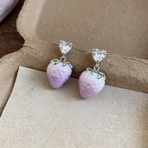 Close-up of sweet strawberry drop earrings with heart crystal studs on rustic background.