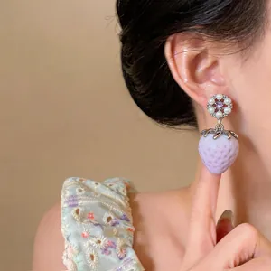 Close-up view of elegant purple strawberry drop earrings with pearl flower studs on a model