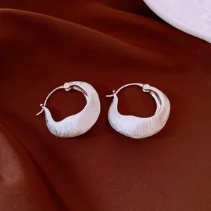 Macro view of 18K gold plated brushed silver-colored hoop earrings on dark silk