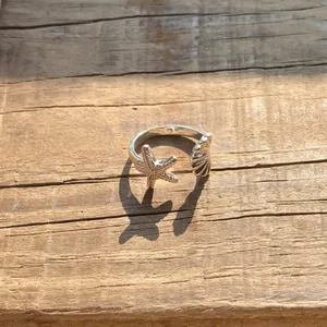 Eleganter silberner Seestern und Muschel offener Ring auf einem rustikalen Holzhintergrund