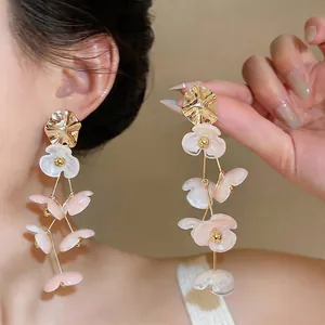 Close-up view of elegant white and pink acrylic flower tassel earrings worn by a model