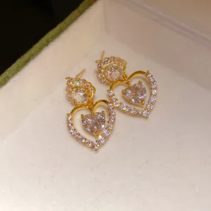 Gros plan de boucles d'oreilles pendantes en zircon à double cœur dorées dans un écrin.