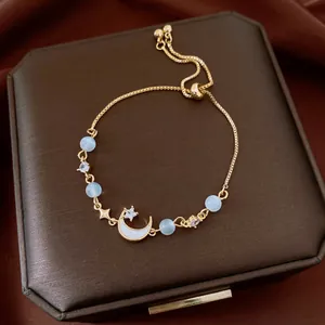 Delicate gold adjustable bracelet featuring zircon moon and star charms with cat eye beads.