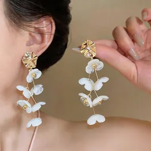 Close-up detail of white acrylic flower tassel earrings with gold metal accents.