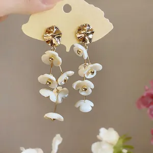 Close-up detail of golden alloy earrings with cascading white acrylic flower petals