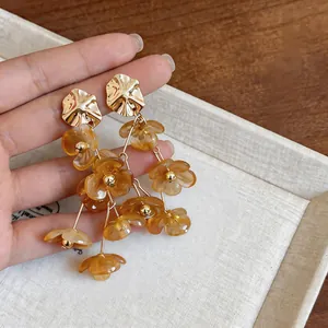 Close-up of elegant dangling amber acrylic flower earrings with gold alloy tassel details