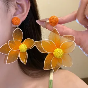 Oversized orange mesh flower petal earrings with yellow center worn by a female model