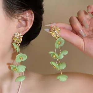 Detail shot of long green acrylic flower tassel earrings with gold wavy studs on a model.