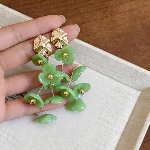 Close-up of green acrylic flower earrings with gold tassel and metallic studs