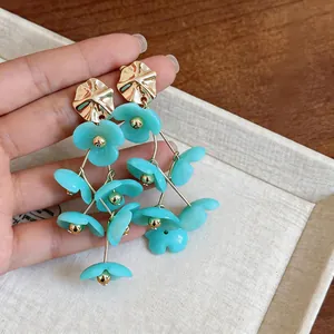 Detail view of blue acrylic flower tassel earrings with gold-finish wavy studs.
