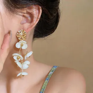 Detailed macro view of oversized white acrylic flower tassel earrings worn by model.