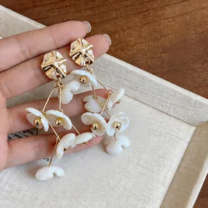 Close-up of gold tassel earrings with white acrylic flowers and metallic studs.