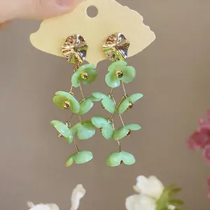 Detail of green acrylic flower tassel earrings with golden metal studs in sweet style.