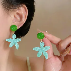 Dettaglio di orecchini boho a forma di stella marina verdi e blu, indossati e in mano.