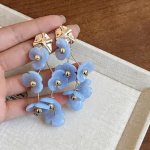 Close-up of light blue acrylic flower tassel earrings with gold-toned metal accents.