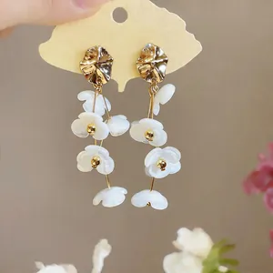Detailed close-up of white acrylic flower tassel earrings with golden irregular studs