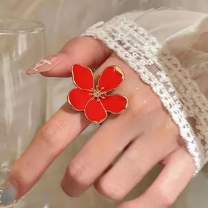 Close-up detail of a large red enamel flower ring worn on a hand with lace sleeve