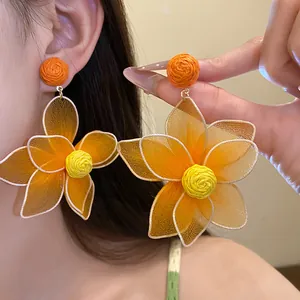 Close-up of vibrant orange mesh flower earrings with woven yellow center detail