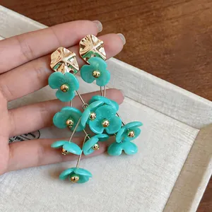 Close-up of green acrylic flower tassel earrings with gold-toned metal details.