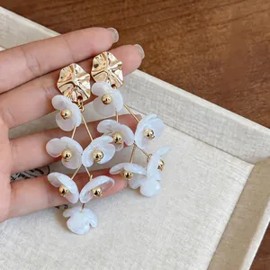 Detailed macro view of white acrylic floral tassel earrings with gold alloy accents