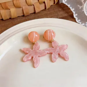 Primo piano di orecchini a forma di stella marina in resina marmorizzata rosa su piatto bianco