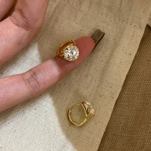 Elegant gold huggie earrings with a large round sparkling cubic zirconia on a finger.