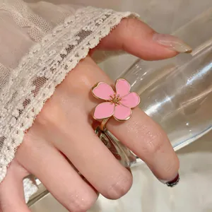 Detailed close-up of a pink enamel flower ring with golden stamen on a model's hand.