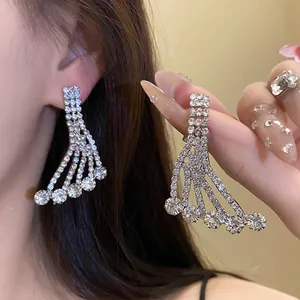 Close-up of sparkling silver rhinestone tassel earrings worn on ear and held by hand