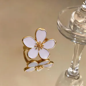 Detail view of an elegant gold flower ring with white enamel petals on a mirror