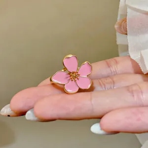 Detail shot of a delicate pink enamel flower ring with gold metal edges on a hand