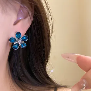 Detailed macro shot of an elegant blue floral earring with crystal petals on a model.