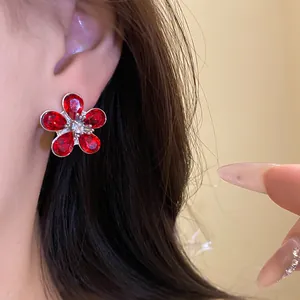 Close-up of elegant red crystal flower stud earring with silver needle worn on ear.