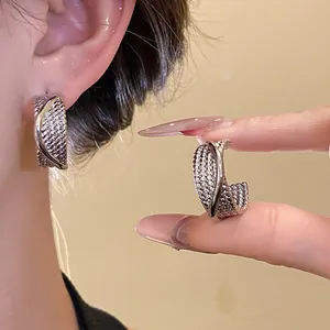 Detailed view of silver textured C-shaped hoop earrings on ear.