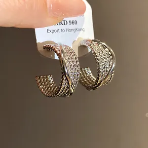 Close-up detail of silver-toned C-shaped hoop earrings with intricate woven texture