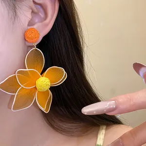 Macro view of large orange mesh flower drop earrings worn on ear showing intricate textures