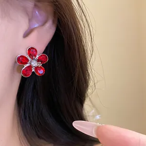 Close-up detail of a silver needle stud earring with red rhinestone flower design.