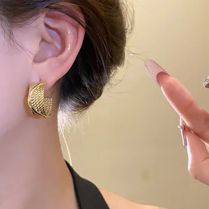 Detailed close-up shot of elegant golden textured C-shaped hoop earrings worn on ear