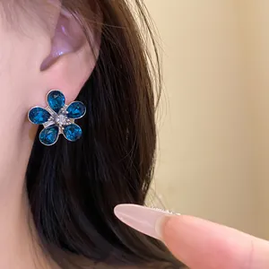 Close-up of elegant floral stud earrings with deep blue gemstones and silver needle