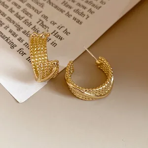Detailed macro view of elegant gold C-shaped hoop earrings with a retro woven texture