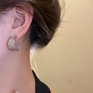 Close-up detail of stylish textured silver-colored C-shaped hoop earrings on ear