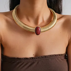 Close-up of a vintage gold ribbed collar necklace featuring a central red resin stone