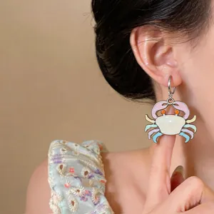 Detail of a colorful enamel crab drop earring worn by a model in a studio setting.