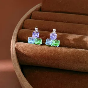 Close-up of geometric earrings with purple, blue, and green glass stones in a velvet tray